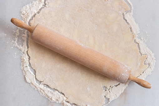 Fresh pastry dough being rolled out with a rolling pin in the kitchen on a marble pastry board