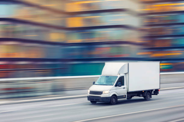 Fast delivery truck travelling through the city streets A delivery truck travelling fast on a city street with motion blurred office buildings in the background. delivery person stock pictures, royalty-free photos & images