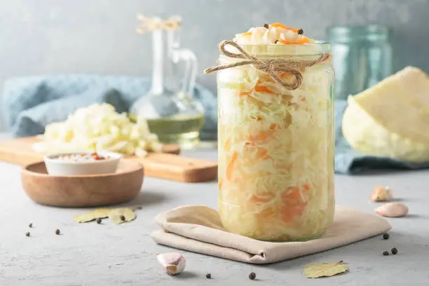 Sauerkraut in a glass jar with ingredients on a concrete background.