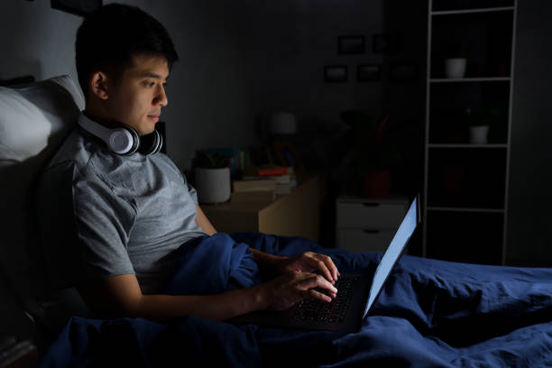 Young man using a laptop in his bed at night