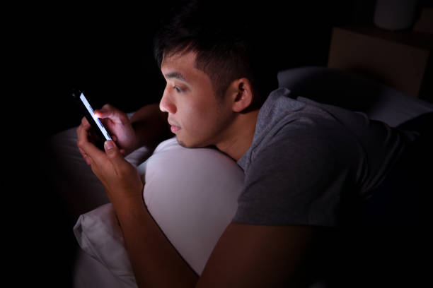 istock Young man having sore and tired eyes when using a smartphone while lying in bed at night 1292258622