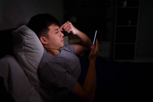 istock Young man having sore and tired eyes when using a smartphone while lying in bed at night 1292258623