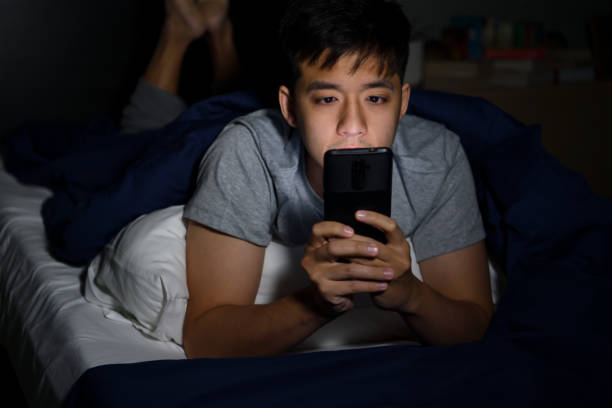 istock Young man having sore and tired eyes when using a smartphone while lying in bed at night 1292258625