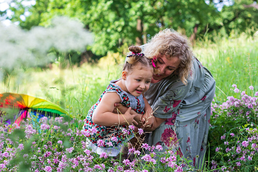 a young mother and her little daughter are having fun happy on a green flower meadow in a Park on a summer day