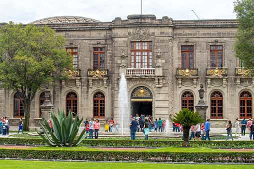 People walking next to a water fountain at the entrance of the Chapultepec Castle at Mexico city, Mexico.