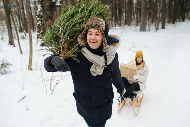 istock Man carrying fir tree and pulling sleigh with his girlfriend in a snowy forest 1292260578