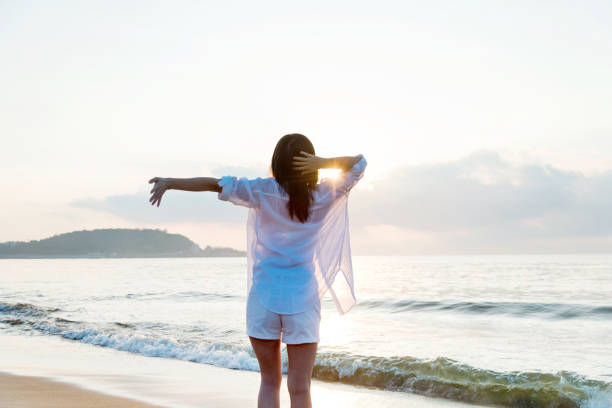 istock Young woman standing on beach with arms outstretched 1292261056