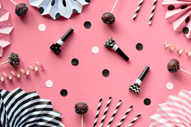 Yummy eclairs or brewing cakes and cake pops covered with chocolate and colorer sugar icing. Creative monochrome top view on pink color paper decorated with paper fans, confetti, party blowers