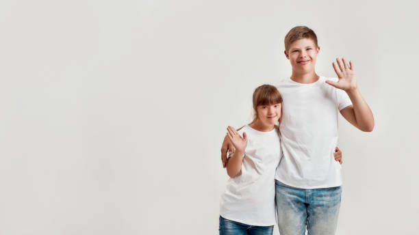 Two kids, disabled boy and girl with Down syndrome smiling and waving at camera, embracing each other while posing together isolated over white background Two kids, disabled boy and girl with Down syndrome smiling and waving at camera, embracing each other while posing together isolated over white background. Children with disabilities and special need down syndrome photos stock pictures, royalty-free photos & images
