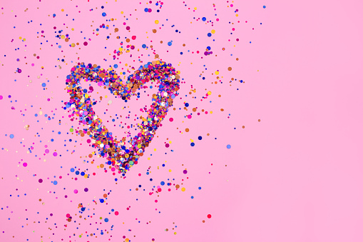 Heart made from explosion of shiny colorful sparkles on bright pink background with copyspace for your text. St. Valentine's day or birthday concept. Selective focus