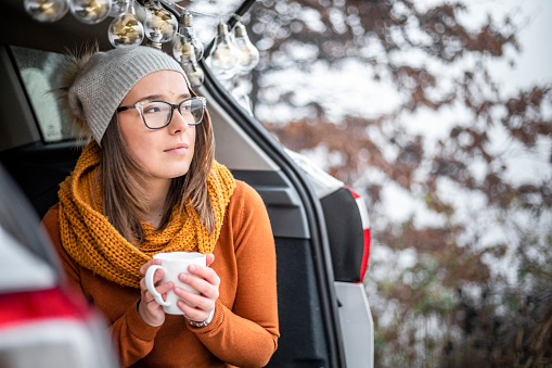 Winter day in nature - A young woman sitting in a car and drinking tea - A break from traveling