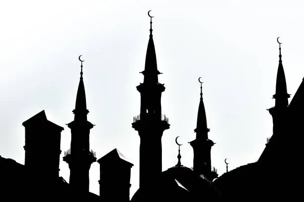 Black silhouette of a Muslim mosque against a bright sky. Towers of the mosque with a Crescent.