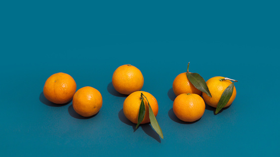 Clementines fruit with green leaves close-up on a blue teal color background. Trendy food mockup with mandarins and sharp shadows. Minimal composition of citrus with copy space, winter vitamins.