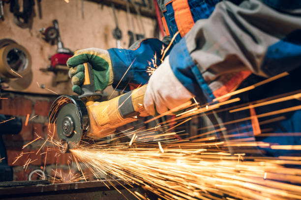 istock Locksmith in special clothes and goggles works in production. Metal processing with angle grinder. Sparks in metalworking 1292277756