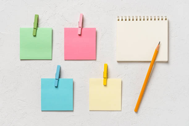 istock Four colorful blank post-it notes every with wooden clothespin and spring notepad with pensil on a white concrete background. Plan tasks, share ideas, creativity concept. 1292280232