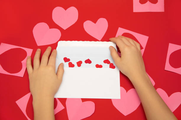 istock Valentine's day message in white envelope on red background. Human hands fold hearts valentines 1292286729