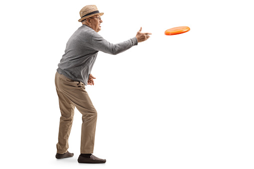 Full length profile shot of an elderly gentleman throwing a frisbee isolated on white background