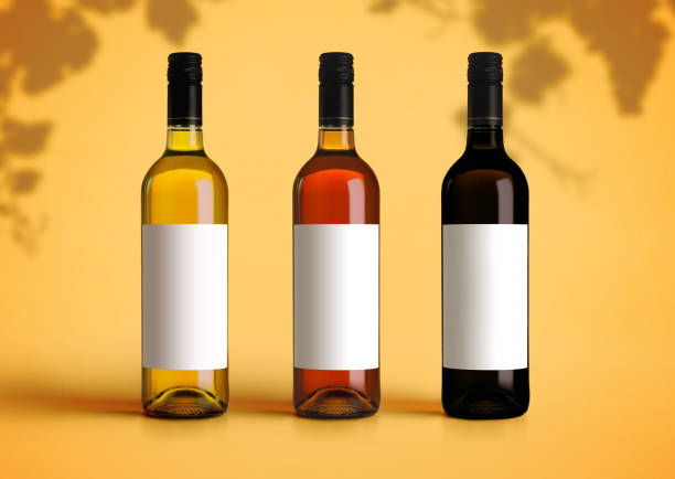 maquette de plan rapproché de trois types de bouteilles de vin sur un bureau et un fond jaunes. modèle vide de papier blanc pour insérer votre marque ou conception - bottle wine red blank photos et images de collection