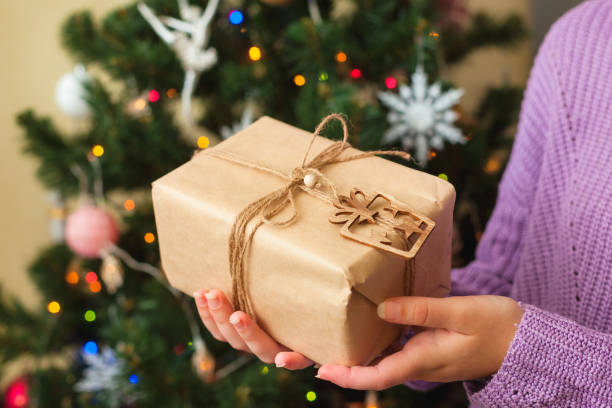 istock Womans hands holding nice present, decorated Christmas tree on background 1292290642