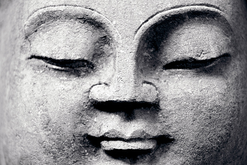 Closeup face of Buddha, old stone statue, front view, black and white, copy space, full frame horizontal composition