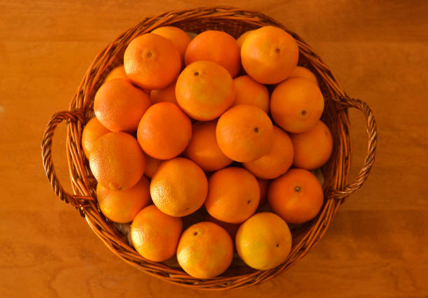 Top view of clementines in a wicker basket on a wooden table.