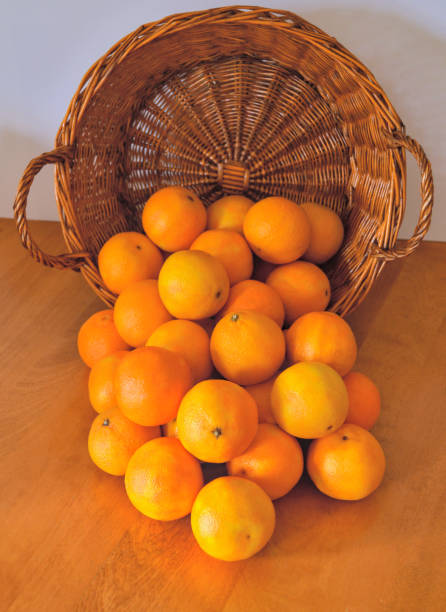 Bunch of clementines falling from a wicker basket on a wooden table stock photo