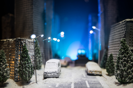 Little miniature city with road and lights. Decorative cute small houses in snow at night in winter. Creative Holiday concept. Christmas and New Year attributes decorated composition.