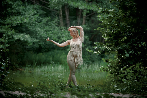 Beautiful young blonde woman in full growth. In the woods in summer. Clothing of their eco-materials and macrame. The concept of natural products and harmony with nature.