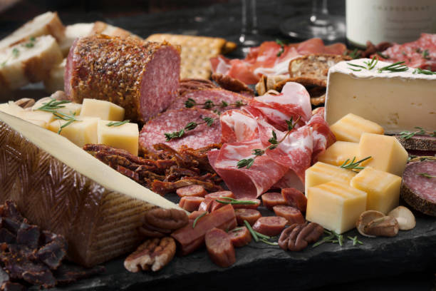 Charcuterie Board Cured Meat and Cheese Platter with Nuts, Crackers, Crusty Bread and White Wine prosciutto stock pictures, royalty-free photos & images