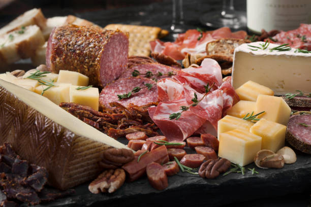 Charcuterie Board Cured Meat and Cheese Platter with Nuts, Crackers, Crusty Bread and White Wine prosciutto brie stock pictures, royalty-free photos & images