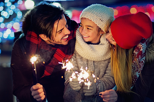 Woman with gray sweater holding a sparkling sparkler in her hands on blurred background, close up, Christmas celebration concept.