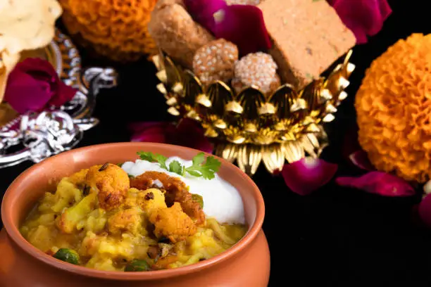 Photo of Close Up Details Of Delicious Daliya Dal Khichdi Served In Traditional Indian Matka With Curd And Til Gul Gur Ke Gajak And Floral Decoration. Makar Sankranti Lohri Pongal Celebration Theme Of Hindu