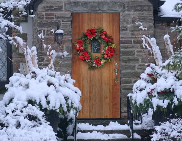 Photo of Old wood grain front door with Christmas wreath and snow covered trees