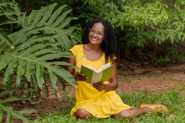 Young black woman sitting on lawn reading book.