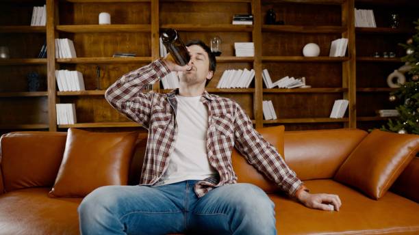 istock Alcohol addiction at young age. Caucasian male cannot stop drinking alcohol, drunken lonely male drinks wine from bottle. Loneliness, depression and alcoholism during Christmas and New Year holidays 1292312542
