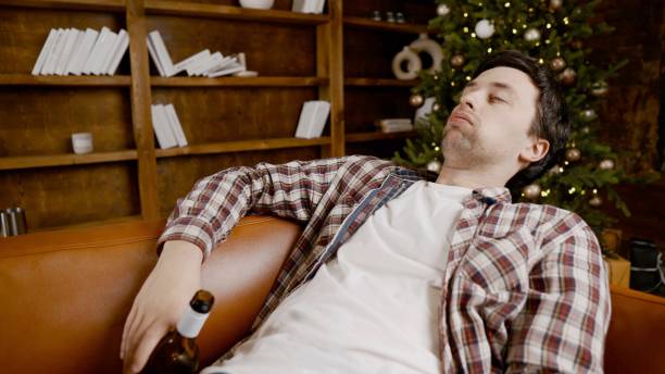 Alcohol addiction at young age. Caucasian male cannot stop drinking alcohol, drunken lonely male drinks wine from bottle. Loneliness, depression and alcoholism during Christmas and New Year holidays