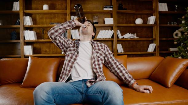 Alcohol addiction at young age. Caucasian male cannot stop drinking alcohol, drunken lonely male drinks wine from bottle. Loneliness, depression and alcoholism during Christmas and New Year holidays