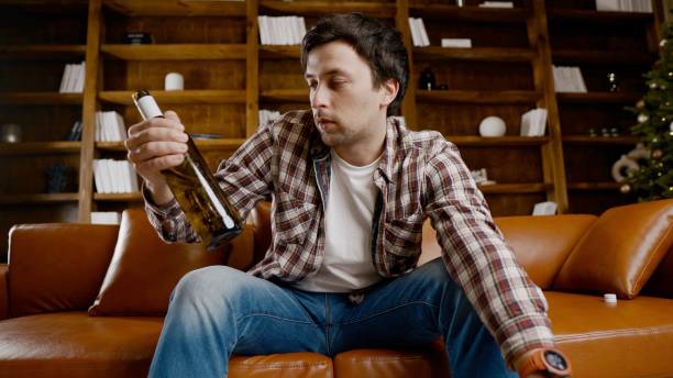 istock Alcohol addiction at young age. Caucasian male cannot stop drinking alcohol, drunken lonely male drinks wine from bottle. Loneliness, depression and alcoholism during Christmas and New Year holidays 1292315220