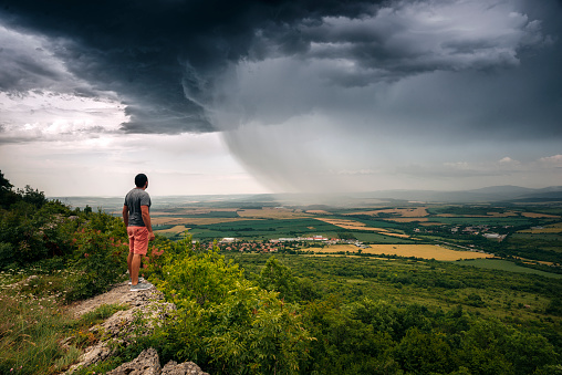 Man standing on the edge of the cliffs and watching a nice structured storm in the summer fields