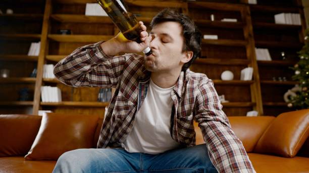 istock Alcohol addiction at young age. Caucasian male cannot stop drinking alcohol, drunken lonely male drinks wine from bottle. Loneliness, depression and alcoholism during Christmas and New Year holidays 1292315710