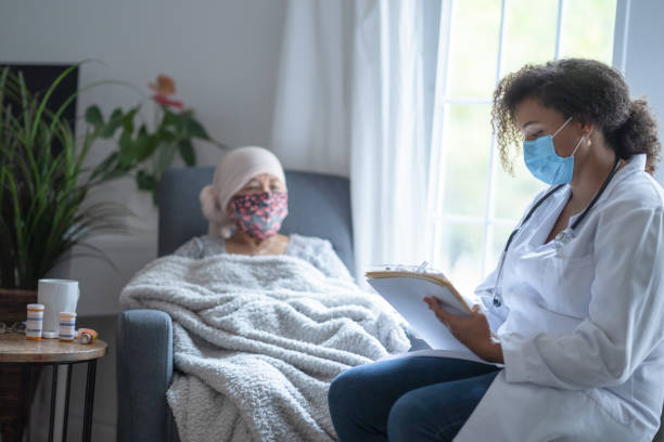 Senior asian female cancer patient wearing mask talking to doctor In a hospital room, an asian female cancer patient is chatting with her doctor. Both of them are wearing a mask during the coronavirus pandemic to help prevent the transfer of germs. The doctor is a female and of African American ethnicity. chemotherapy drug stock pictures, royalty-free photos & images