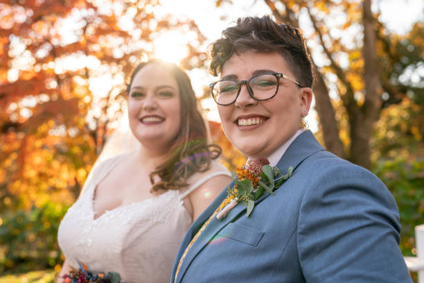 We're married! A young and beautiful lesbian couple smile directly at the camera while celebrating their marriage at an outdoor reception party on their wedding day. free wedding stock pictures, royalty-free photos & images