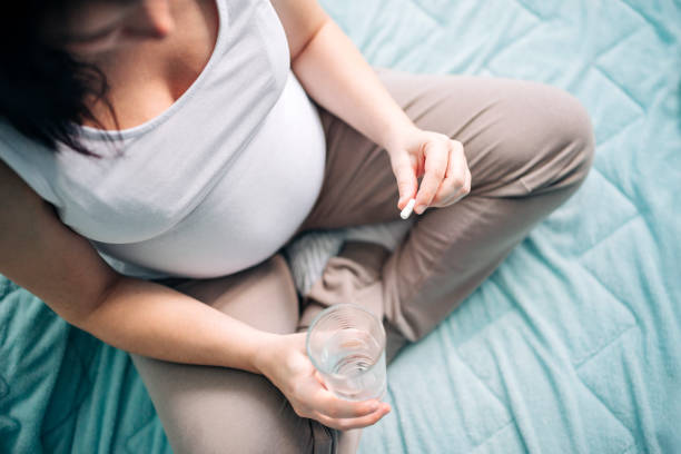 femme enceinte prenant la pillule à la maison - ion photos et images de collection