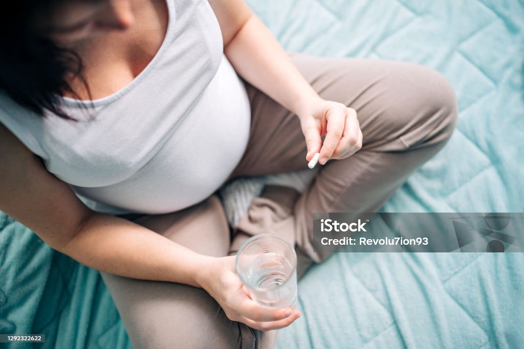 Pregnant woman taking pill at home Young pregnant woman holding pills in hand Pregnant Stock Photo