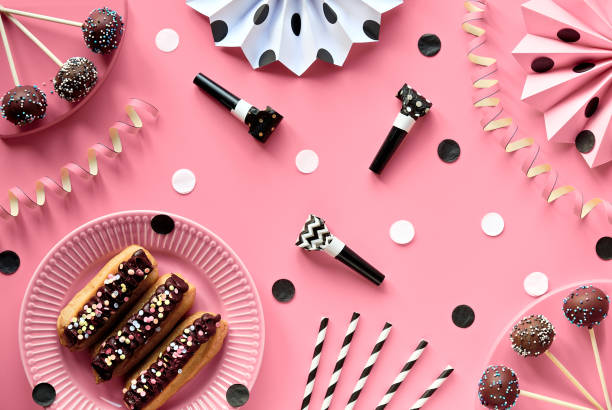 istock Yummy eclairs or brewing cakes and cake pops covered with chocolate and colorer sugar icing. Creative monochrome flat lay on pink color paper decorated with paper fans, confetti, party blowers 1292326049