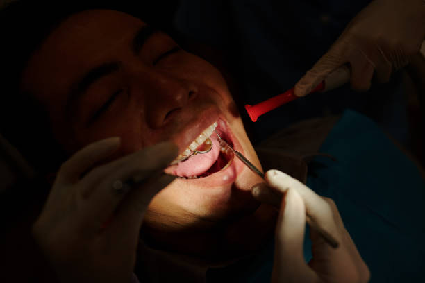 Close-up image of dentist checking front teeth of male patient with mouth mirror and carver