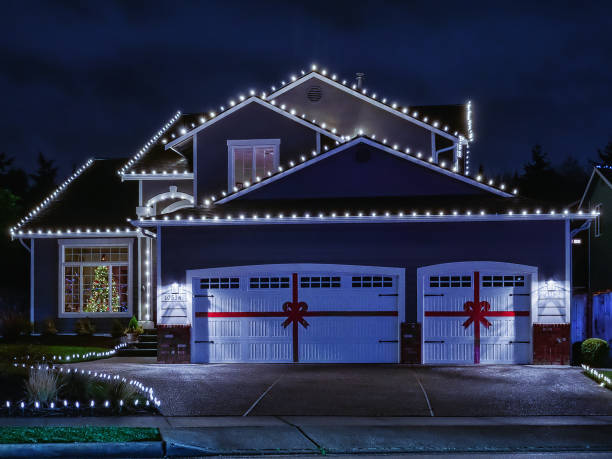 American suburban home exterior with festive Christmas lights Night time photo of a modern American suburban home decorated with festive Christmas holiday lights and red ribbons on garage doors christmas lights house stock pictures, royalty-free photos & images