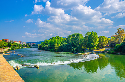 Po river in Turin city historical centre with water dam and green trees on shore, blue sky white clouds