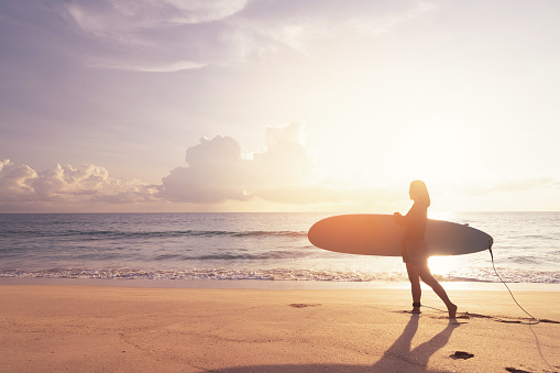 Woman hold surfboard standing at tropical sunset beach background. Summer vacation and sport adventrue concept. Vintage tone filter effect color style.