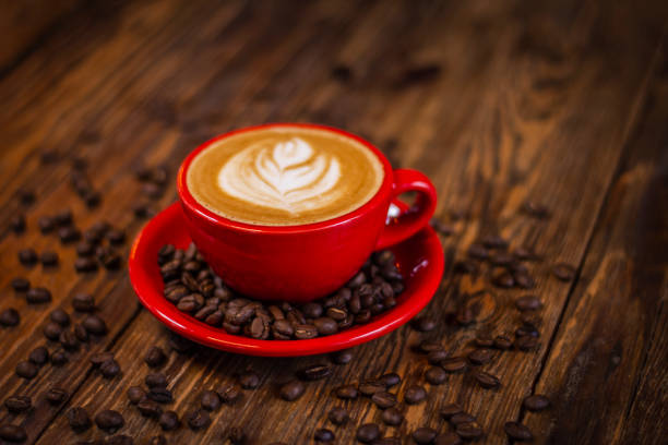 istock Hot cappuccino coffee in red cup with saucer on wooden table 1292362995